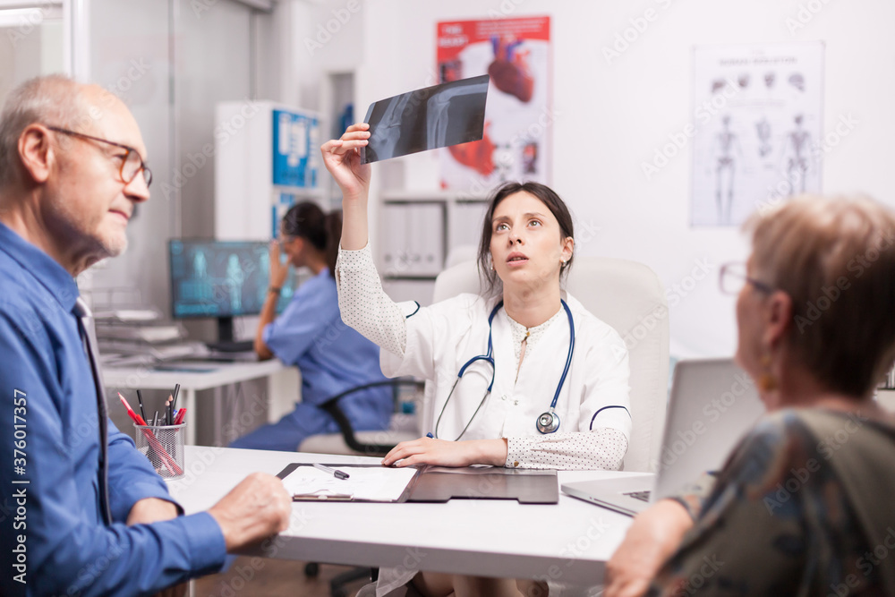 Female doctor looking at senior patient x-ray during consultation after surgery. Medic examining radiography in hospital office. Nurse working on computer. Female doctor looking at senior patient x-ray during consultation after surgery. Medic examining radiography in hospital office. Nurse working on computer.