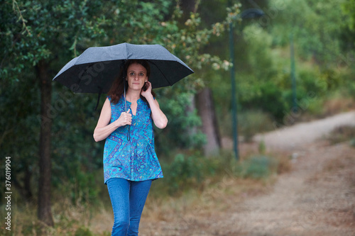 woman walking in the rain with black umbrella in rural setting