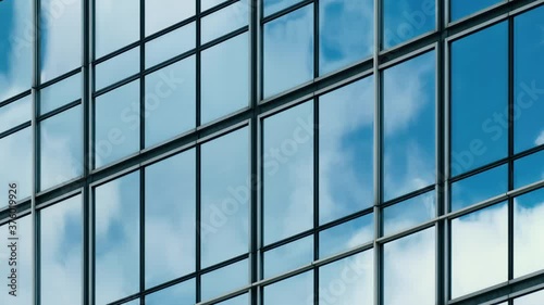 Time lapse of blue sky and clouds reflected in structural modular glass wall. Tilt shot.