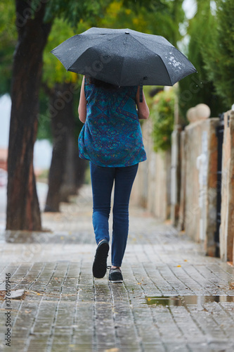 woman walking in the rain with black umbrella in rural setting