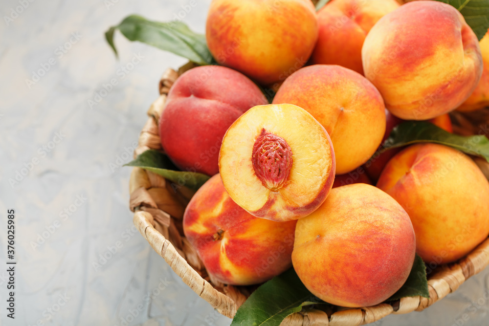 Ripe peaches in a wicker basket on a stone gray table with a juicy peach slice with a stone pit.