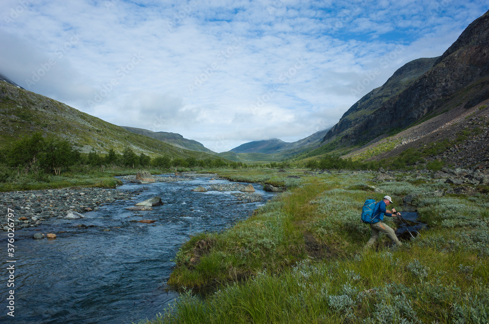 Hiking in Swedish Lapland. Man with backpack crossing river trekking alone in Vistasvagge valley in northern Sweden. Arctic mountain nature of Scandinavia in summer day