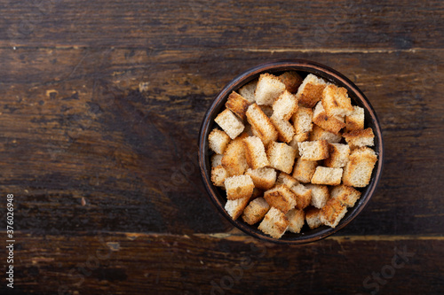Crispy croutons in a bowl on a wooden background.