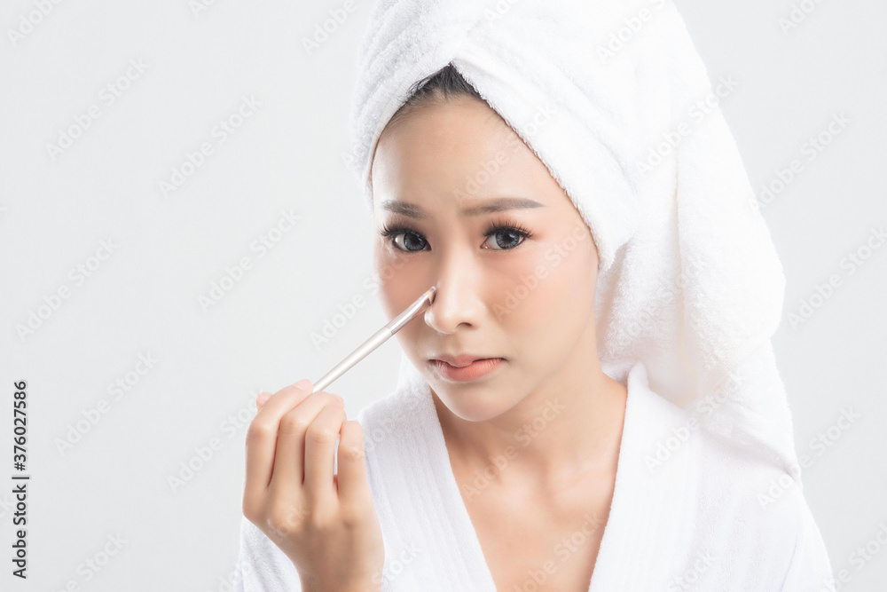 Beautiful young woman wearing bathrobe with towel with towel on head is using a makeup brush makeup her after bathing, at studio shot isolated on white background.
