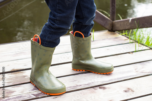 Child wearing gumboots standing on wooden bridge by the river, the concept of recreation and autumn.