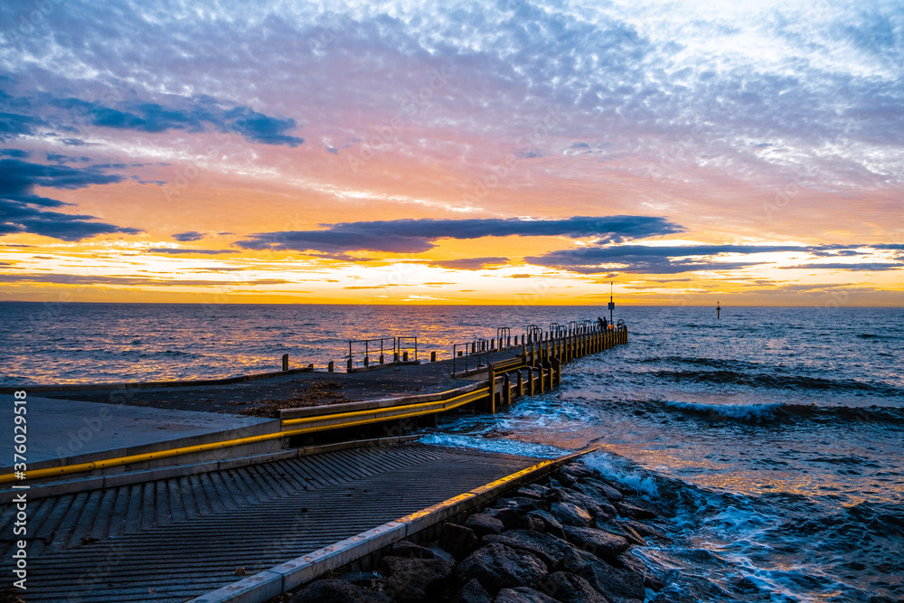 Obraz premium Beautiful glowing sunset over ocean and small boat jetty in Melbourne, Australia
