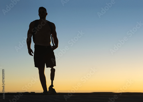 Fototapeta Naklejka Na Ścianę i Meble -  Silhouette of athletic man with prosthetic leg with sunset sky at background