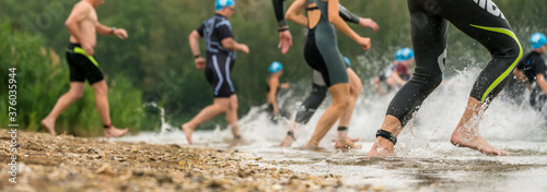 Athletes in wetsuits running into a lake at a triathlon competition