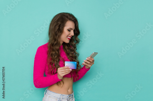 Young Smiling Woman Holds Credit Card And Looks At Telephone