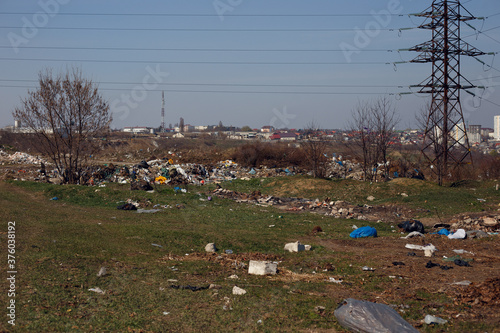 Field covered with garbage, tires and plastic bags thrown and scattered on the city background.