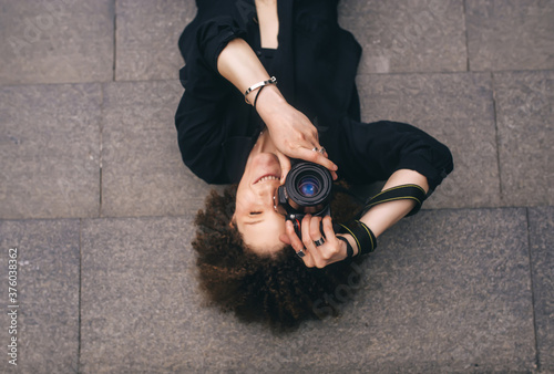 Brunette woman with digital 50mm lens reflex camera is lying on the steps. Top view photo