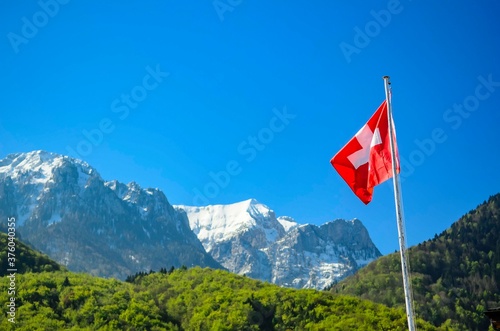 The Swiss flag fluttering on the background of the sky and the Swiss Alps. Switzerland