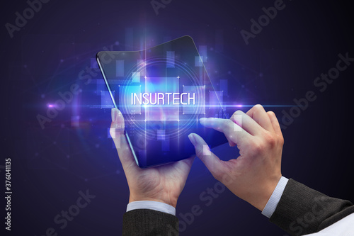 Businessman holding a foldable smartphone with INSURTECH inscription, new technology concept