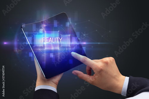 Businessman holding a foldable smartphone with REALITY inscription, new technology concept