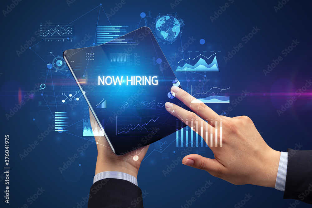 Businessman holding a foldable smartphone with NOW HIRING inscription, successful business concept Businessman holding a foldable smartphone with NOW HIRING inscription, successful business concept