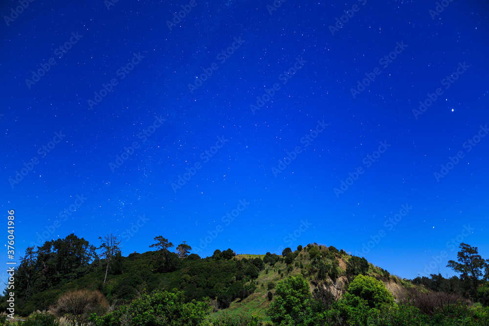 A starry night sky above a moonlit country landscape in New Zealand. The Southern Cross is at center left and Jupiter shines brightly to the far right A starry night sky above a moonlit country landscape in New Zealand. The Southern Cross is at center left and Jupiter shines brightly to the far right
