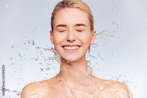 Photo of  young  woman with clean skin and splash of water. Portrait of smiling woman with drops of water around her face. Spa treatment. Girl washing her body with water. Water and body.