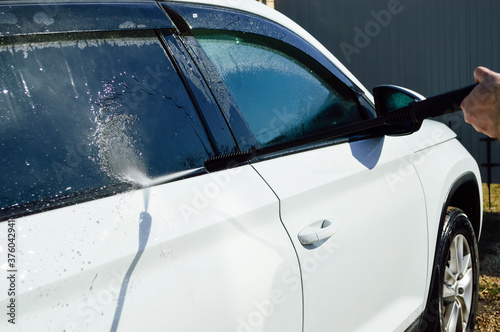 close-up - a man holding a high pressure car wash gun in his hands  washes the body of a white car and glass