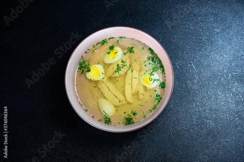 Soup with noodles, chicken, egg and dill on a dark background in a plate