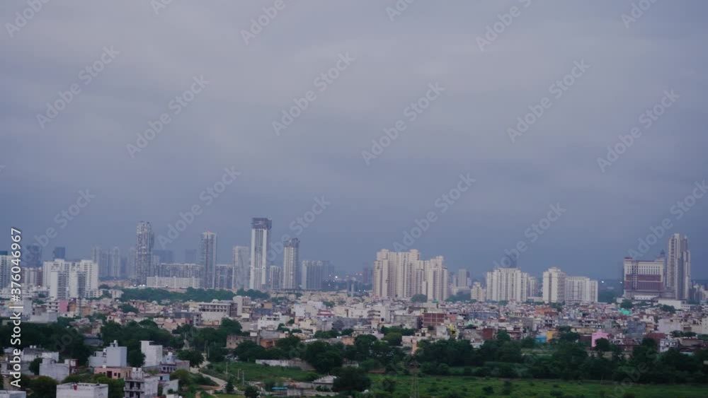 aerial shot from day to night showing the cityscape of gurgaon with feilds, small houses, skyscrapers in the background aerial shot from day to night showing the cityscape of gurgaon with feilds, small houses, skyscrapers in the background