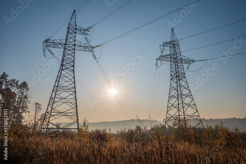 Two high voltage power lines go into the distance. Against the background of the sky and the bright sun.