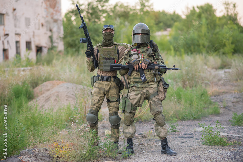 A professional airsoft player stands in a big helmet and a machine gun and with his partner