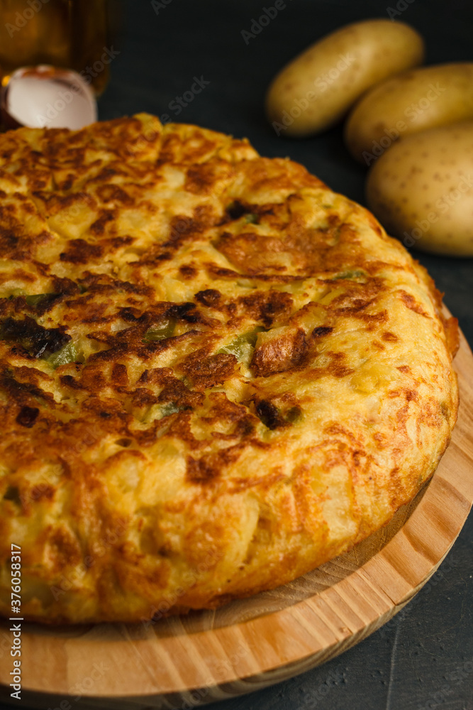 Tortilla de Patatas served on a wood board. Traditional Spanish dish with eggs, potatoes, onion, olive oil and green peppers. Rustic black background. Tortilla de Patatas served on a wood board. Traditional Spanish dish with eggs, potatoes, onion, olive oil and green peppers. Rustic black background.