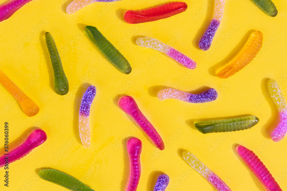 Yellow, purple, red, pink and green sugar coated jelly worms pattern on a yellow background Yellow, purple, red, pink and green sugar coated jelly worms pattern on a yellow background