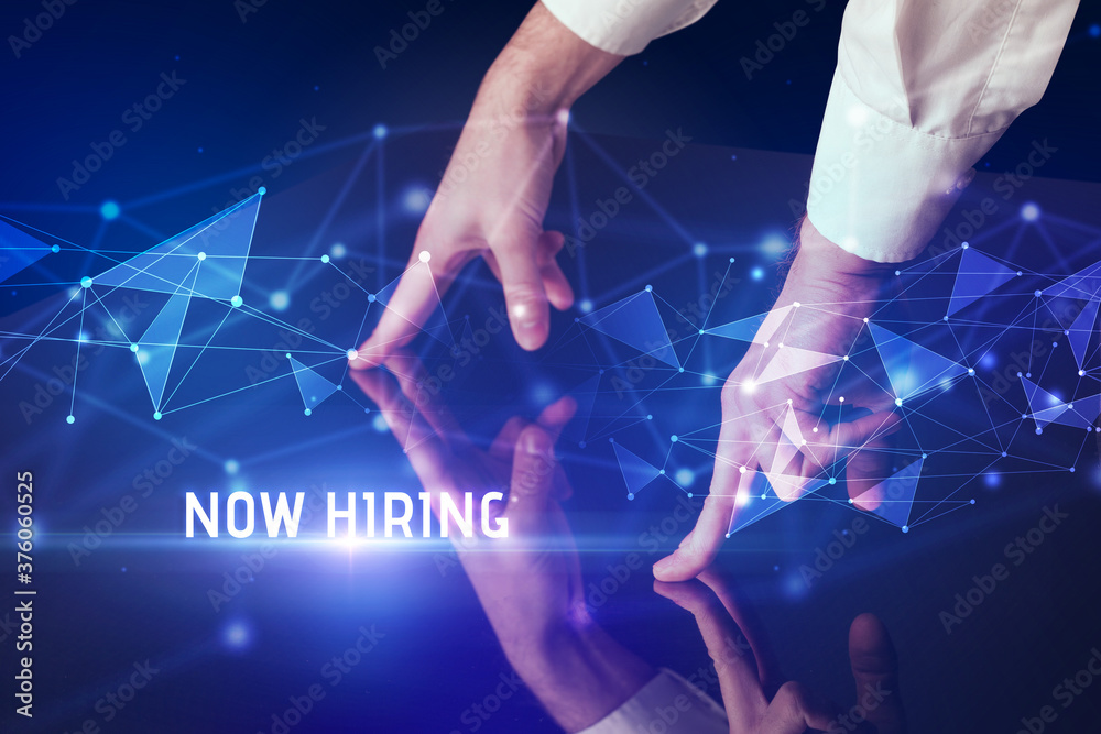 Businessman touching huge screen with NOW HIRING inscription, modern technology business concept Businessman touching huge screen with NOW HIRING inscription, modern technology business concept