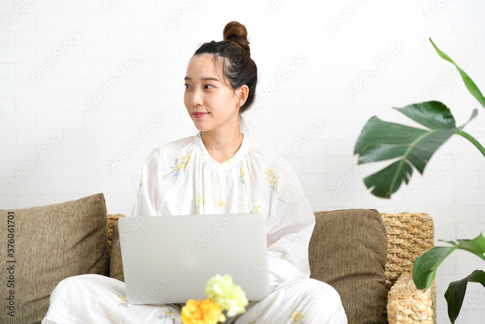ソファーの上であぐらをかいてパソコンを操作する女性 ソファーの上であぐらをかいてパソコンを操作する女性