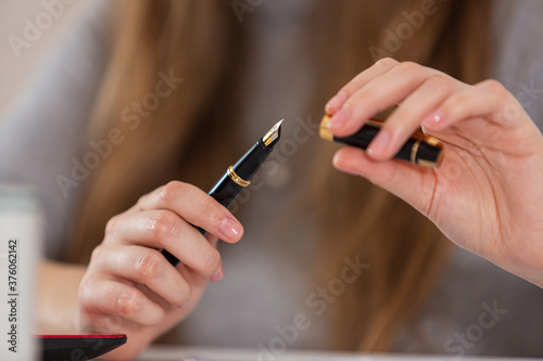 Black fountain pen being used by woman against blurry blonde hair. Signing documents. Signature. Close-up.