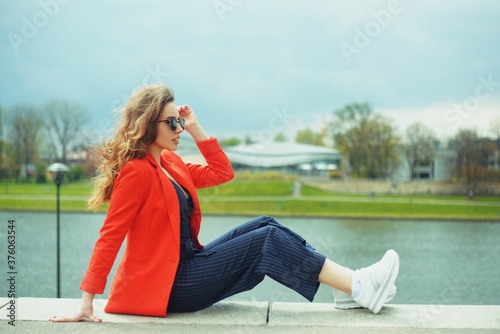 A girl sits at the pier on the background of the river in autumn clothes. © MoreThanProd