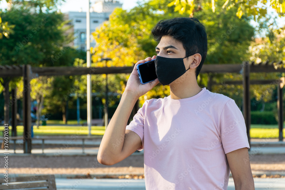 Young man talking on the phone with a medical mask at the park