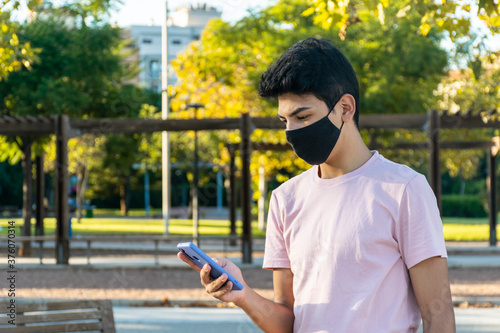 Young man wearing a medical mask using her phone at the park.