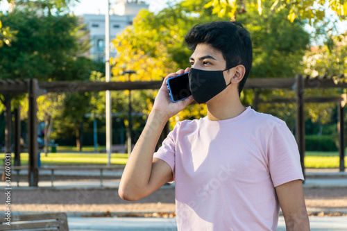 Young man talking on the phone with a medical mask at the park