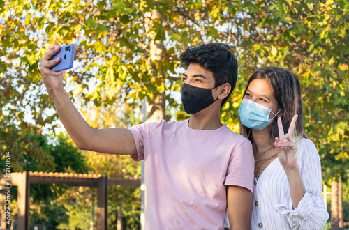 Girl and boy with face masks taking a selfie with a smartphone