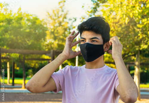 Young man putting on his medical mask on a park