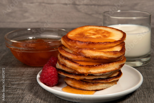 Several pancakes with apricot jam, raspberry and glass of milk on wood background