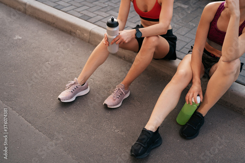 Two women before urban workout. Girls preparing for running and sitting in the street. Fitness break