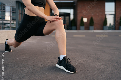 Athlete woman preparing for running on the city street. Legs warming and stretching. Sport tight clothes. Horizontal. 30s