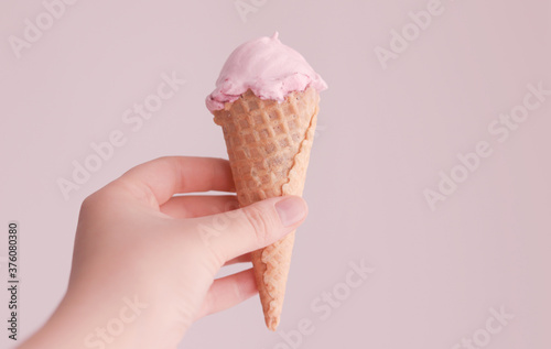 Waffle crunchy cone with pink ice cream in a woman's hand. Selective focus. Pastel pink toning color.