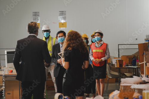 Manager and warehouse work team discuss preventive measures, spaced distance, wear anti-virus masks, workers in warehouse concept.