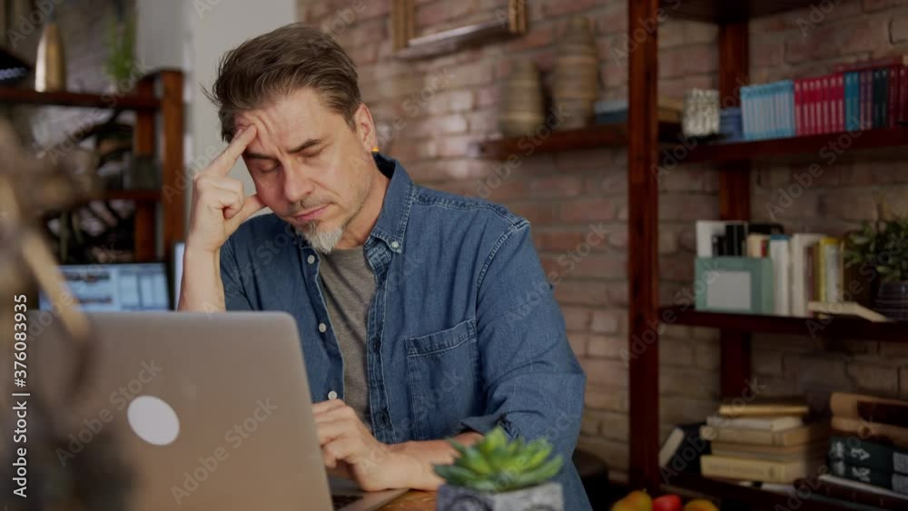 Serious older man working at home with laptop computer sitting at desk in home office. Serious older man working at home with laptop computer sitting at desk in home office.