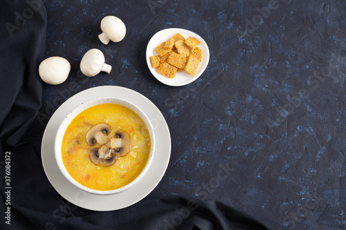 Champignon soup in a white bowl on dark textile. Top of the soup is decorated with slices of sliced mushroom. Flat lay with place for text on dark blue background.