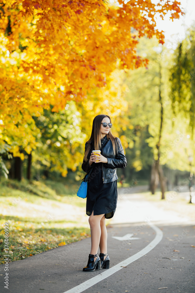 Girl drinks a warming hot drink while walking in the autumn in the park. Holds a cup in his hand against the backdrop of a beautiful autumn park.