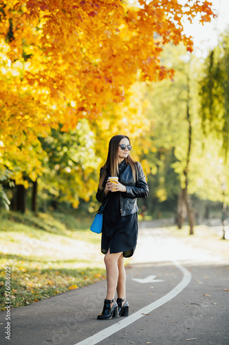Obraz na płótnie Girl drinks a warming hot drink while walking in the autumn in the park. Holds a cup in his hand against the backdrop of a beautiful autumn park. w salonie