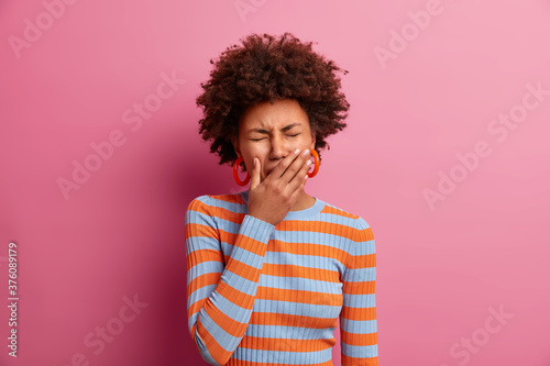 Grieved displeased Afro American woman covers eyes  cries from despair  has frustrated face expression  wears casual striped jumper  has big problem  depressed over something. Emotional burnout