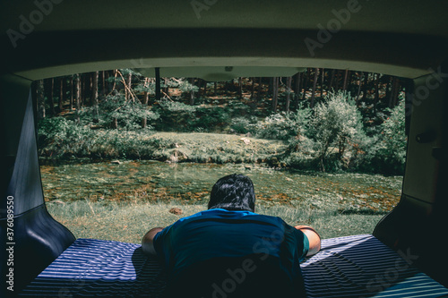 Man looking views from the mattress of the van to the river photo