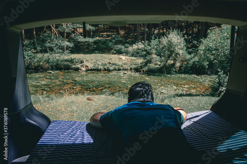 Man looking views from the mattress of the van to the river photo