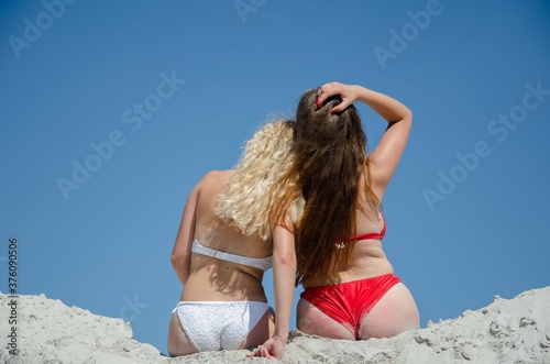 Two girls in swimsuits sitting on the sand. Silhouettes of women sand resort vacation.
